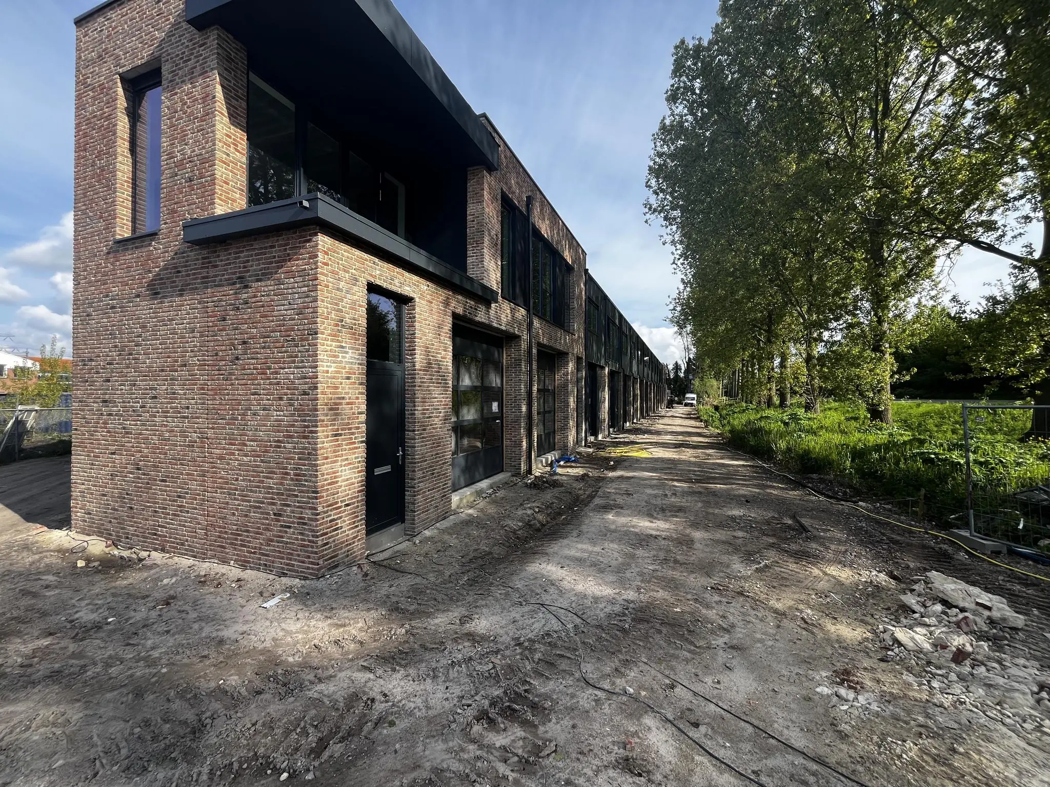 Rij nieuwbouwwoningen aan de Broekdijk West in aanbouw, naast een onverharde weg en groene bomenrij.